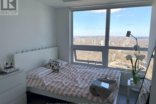 Bedroom with a queen bed, dresser, and large window providing expansive city views. - 4010 - 395 Bloor Street E, Toronto