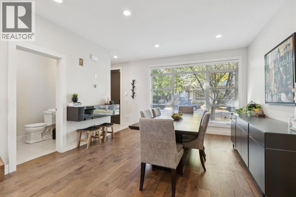 Dining room with a table for six, a large window overlooking trees, and a doorway to a small bathroom. - 4012 2 Street Nw, Calgary