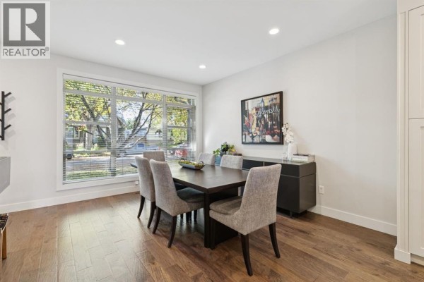 Dining room with a dark wood table, upholstered chairs, buffet, and a large window with blinds. - 4012 2 Street Nw, Calgary