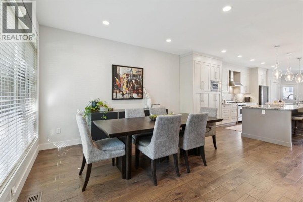 Open-concept dining area adjacent to a kitchen with island, light wood floors, and white cabinets. - 4012 2 Street Nw, Calgary