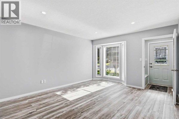 Living room of the duplex with a large bay window, wood-trimmed doors, and blue carpet. - 4014 Shannon Drive, Olds