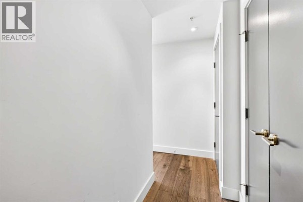 Interior hallway with white walls, wooden floor, and gray doors with brass handles. - 402, 10 Shawnee Hill Sw, Calgary