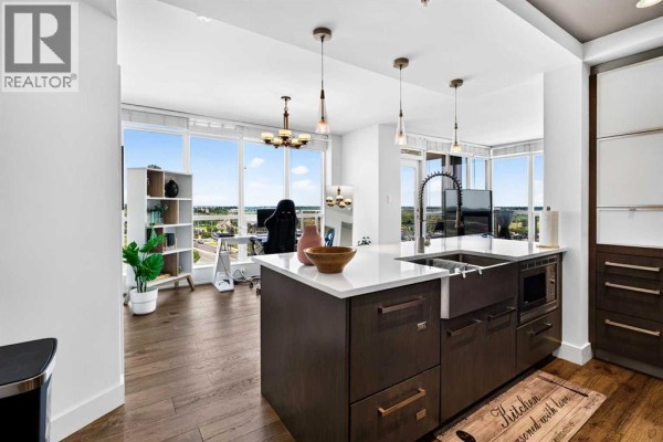 Open-concept living area with kitchen island, stainless steel appliances, and floor-to-ceiling windows. - 402, 10 Shawnee Hill Sw, Calgary