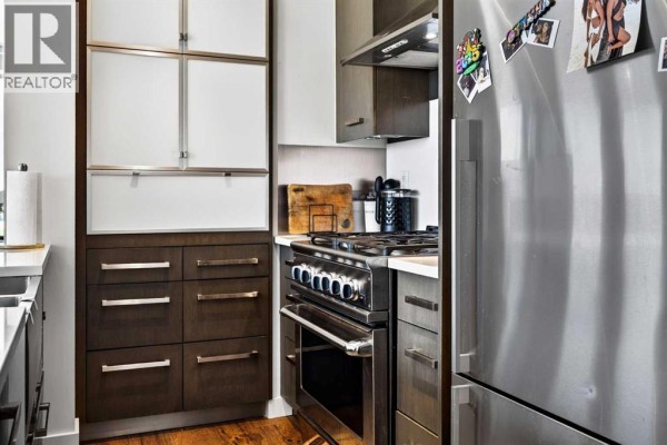 Close-up of a modern kitchen with dark wood cabinets, stainless steel gas range, and oven. - 402, 10 Shawnee Hill Sw, Calgary
