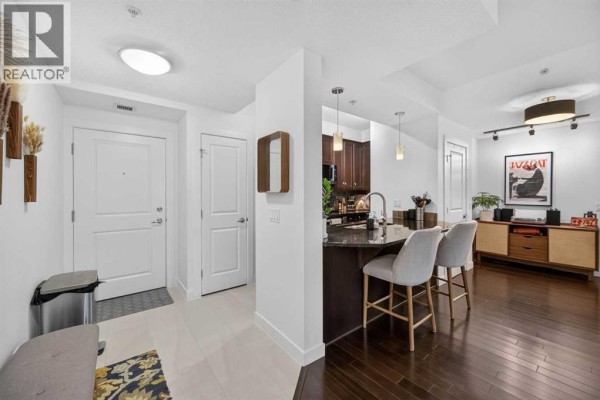 Living room with grey sofa, fireplace, television, and balcony doors with greenery outside. - 402, 108 25 Avenue Sw, Calgary