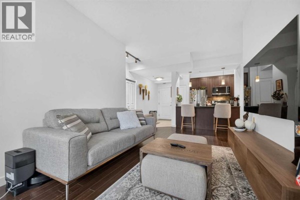 Living room with sofa, ottoman, fireplace, television, and doors to a balcony. - 402, 108 25 Avenue Sw, Calgary