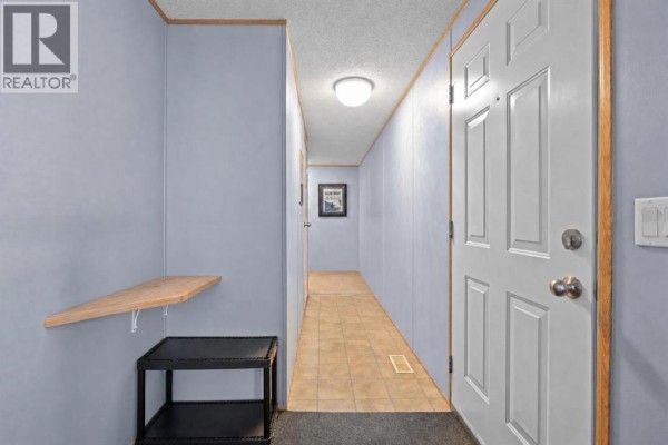 Interior view of a narrow hallway with light blue walls, beige tiled floor, and a white door. - 402, 1101 84 Street Ne, Calgary