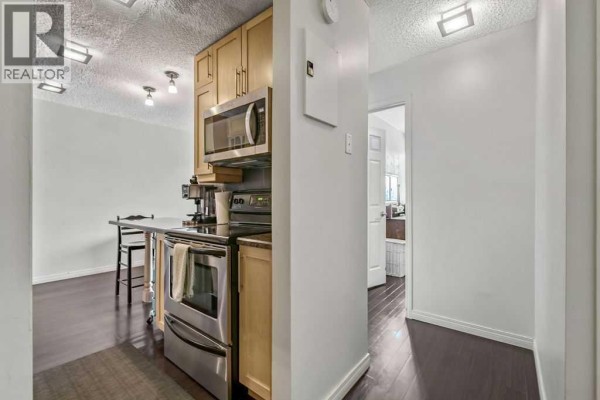 Small kitchen with wood cabinets, stainless steel appliances, and dark flooring. - 402, 2140 17a Street Sw, Calgary