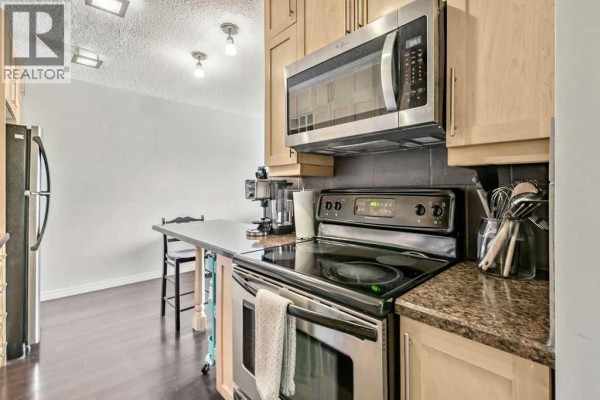 Kitchen with stainless steel oven, microwave, and dark countertop with a small table. - 402, 2140 17a Street Sw, Calgary