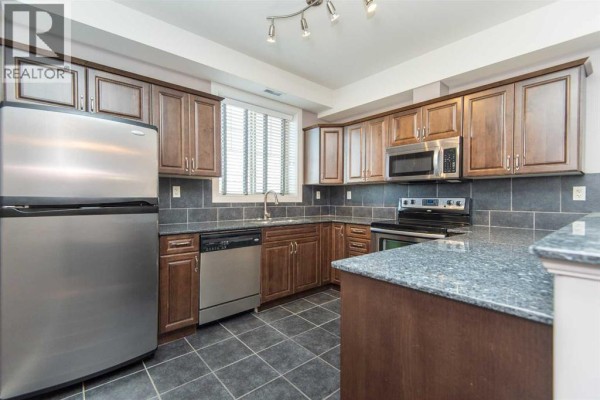 Kitchen with stainless steel appliances, dark wood cabinets, and granite countertops. - 402, 69 Ironstone Drive, Red Deer