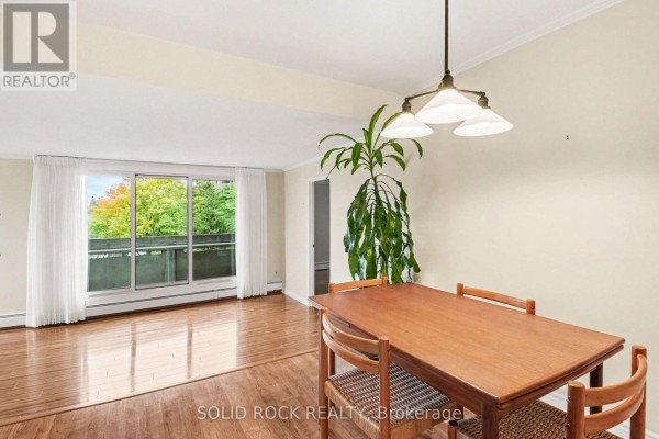 Dining area with a wooden table and chairs, featuring a large window with a balcony view. - 402 - 1171 Ambleside Drive, Ottawa
