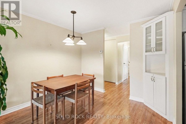Dining area with a wooden table and chairs, and built-in white cabinets with glass doors. - 402 - 1171 Ambleside Drive, Ottawa