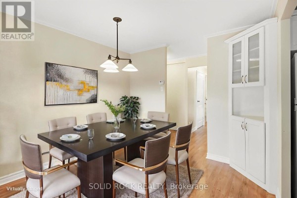 Dining area with a dark table and upholstered chairs, a rug, and a large built-in cabinet. - 402 - 1171 Ambleside Drive, Ottawa