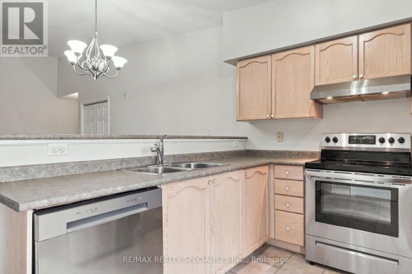 Kitchen counter with sink and dishwasher, overlooking a living area with a chandelier. - 402 - 1470 Bishops Gate, Oakville