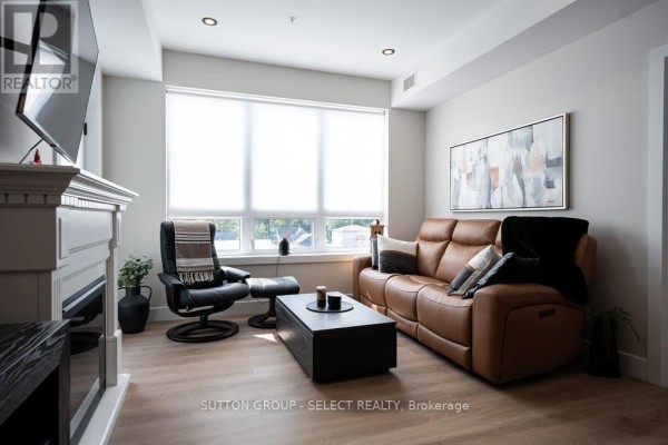 Living room with a brown leather sofa, recliner, fireplace, and large window. - 402 - 15 James Street, South Huron