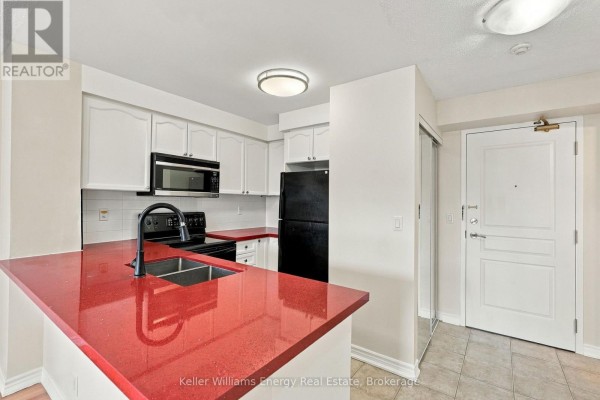 Apartment kitchen with white cabinets, black appliances, and a red quartz countertop island. - 402 - 16 Dallimore Circle, Toronto