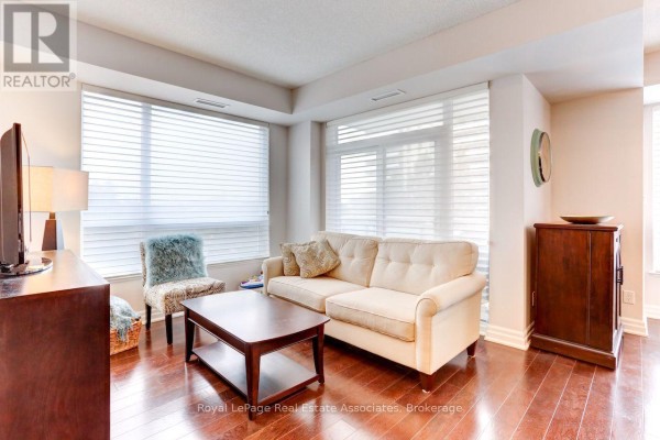 Living room with light beige sofa, wood coffee table, and window blinds. - 402 - 17 Ruddington Drive, Toronto