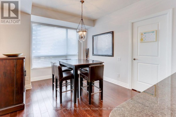 Dining area with a dark wood table, four chairs, and a modern pendant light. - 402 - 17 Ruddington Drive, Toronto