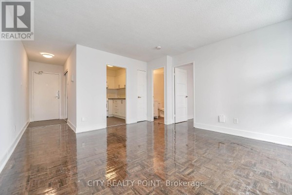 Empty living room with parquet flooring, white walls, and doorway to kitchen and bathroom. - 402 - 33 Isabella Street, Toronto