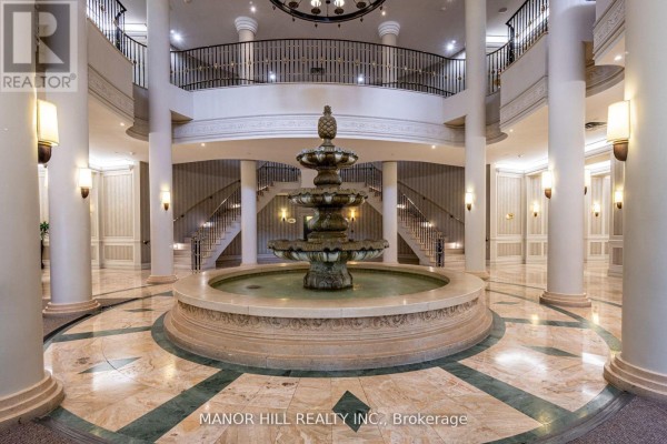 Building lobby with a central tiered fountain, marble floors, columns, and a grand staircase. - 402 - 35 Kingsbridge Garden Circle, Mississauga