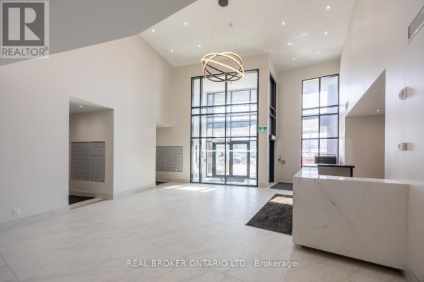 Spacious lobby with white tile floor, modern light fixture, and reception desk. - 402 - 51 Clarington Boulevard, Clarington