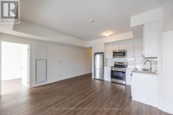 Open-concept living area and kitchen with white cabinetry and stainless steel appliances. - 402 - 51 Clarington Boulevard, Clarington