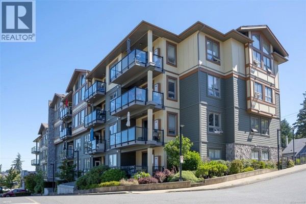 Aerial view of apartment buildings with a lake and forested hills in the background. - 402 3210 Jacklin Rd, Langford