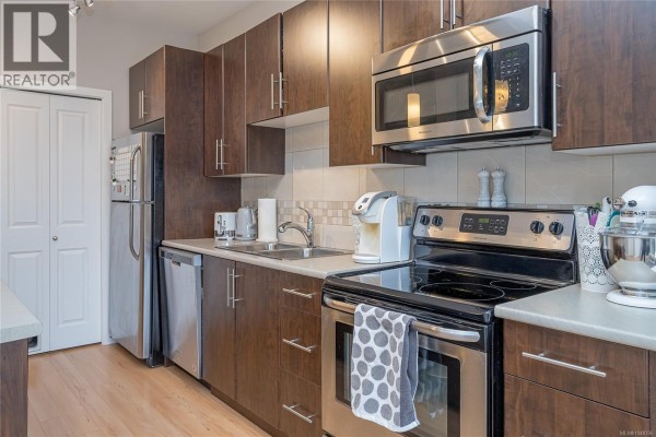 Modern kitchen with stainless steel appliances, island seating, and open layout. - 402 3240 Jacklin Rd, Langford