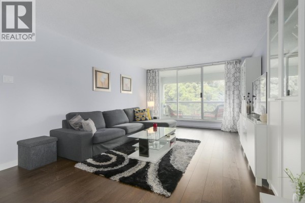 Living room with a grey sectional sofa, coffee table, and view of the balcony. - 402 550 Eighth Street, New Westminster