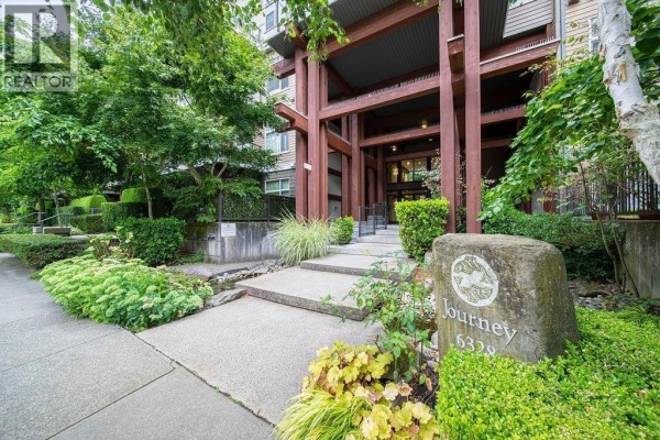 A large balcony with glass railings, overlooking lush green trees and buildings. - 402 6328 Larkin Drive, Vancouver