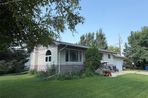 Side view of a beige and grey split-level house with a garden and garage. - 402 Buchanon Avenue, Dauphin