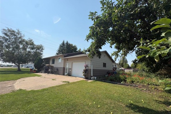 Side view of the house showing a concrete driveway, attached garage, and garden. - 402 Buchanon Avenue, Dauphin