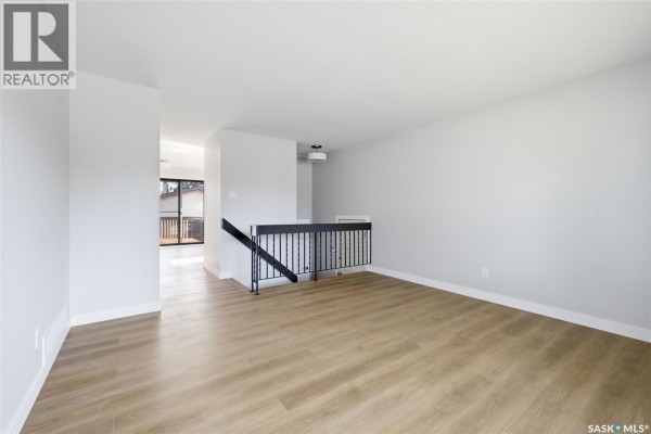 Empty living room with light grey walls, wood floors, and a staircase with black railing. - 402 Fulton Drive, Regina
