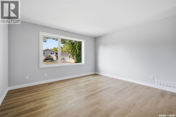 Empty bedroom with light grey walls, wood floors, and a large window with a view of the street. - 402 Fulton Drive, Regina