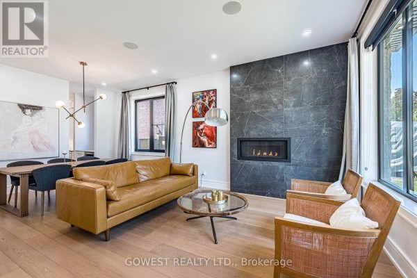 Living and dining area with tan sofa, fireplace, and wooden dining table with grey chairs. - 402 Niar Avenue, Mississauga