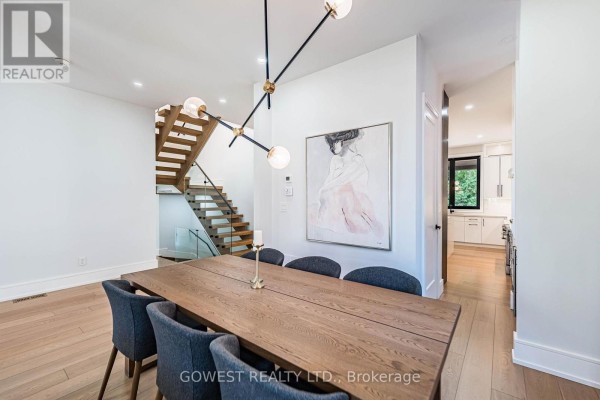 Dining area with large wooden table and grey upholstered chairs, adjacent to open staircase and kitchen view. - 402 Niar Avenue, Mississauga