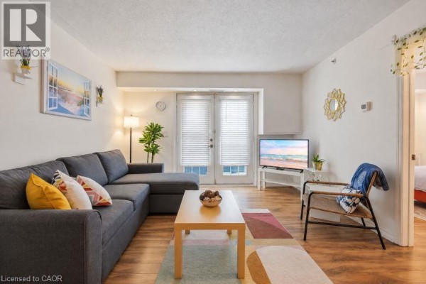 Living room with a grey sectional sofa, patterned rug, television, and double glass doors. - 4025 Kilmer Drive Unit# 310, Burlington
