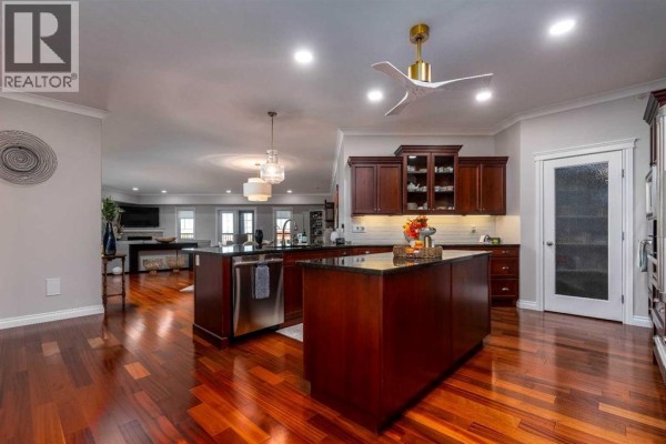 Open concept kitchen with dark wood cabinets, granite countertops, stainless steel appliances, and a large island. - 403, 5305 14 Street, Lloydminster