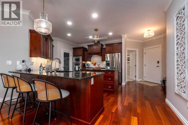 Kitchen island with dark wood base and granite countertop, featuring three bar stools with woven seats. - 403, 5305 14 Street, Lloydminster