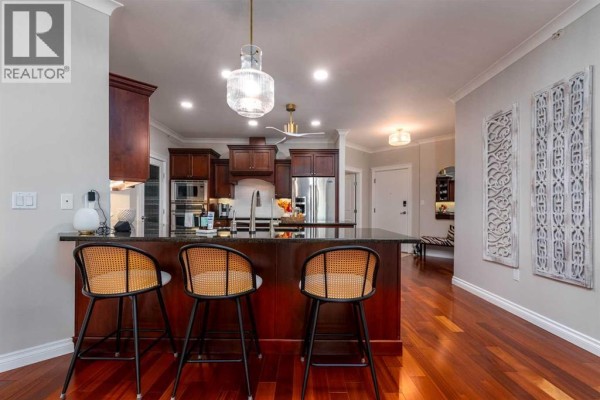 Another view of the kitchen island and breakfast bar area with rattan stools and decorative wall panels. - 403, 5305 14 Street, Lloydminster