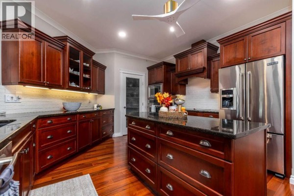Spacious kitchen with abundant dark cherry wood cabinetry, granite countertops, stainless steel refrigerator, and a central island. - 403, 5305 14 Street, Lloydminster