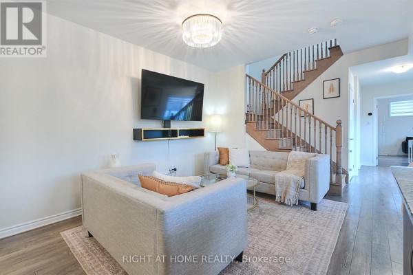 Living room with grey couches, coffee table, television, and wood stairs leading upstairs. - 403 - 1148 Dragonfly Ave Avenue, Pickering