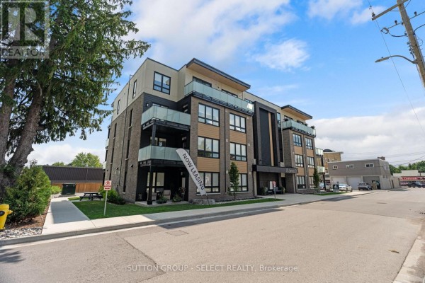 Side exterior view of an apartment building with balconies, trees, and a street. - 403 - 15 James Street, South Huron