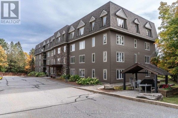 Exterior view of the apartment building showing a paved parking lot and an outdoor covered seating area. - 403 - 24 Dairy Lane, Huntsville