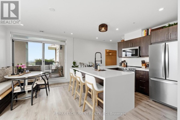 Open concept kitchen and dining area with white island, stainless steel appliances, and balcony access. - 403 - 455 Charlton Avenue E, Hamilton