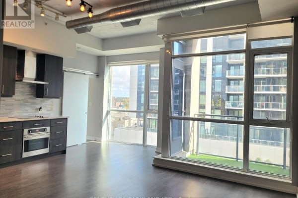 Living area with large windows and balcony overlooking city buildings and a small green space. - 403 - 75 The Donway W, Toronto