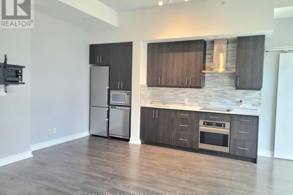 Kitchen area with dark wood cabinets, stainless steel appliances, and a grey tiled backsplash. - 403 - 75 The Donway W, Toronto