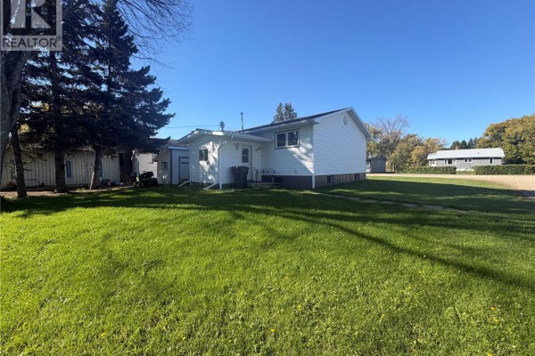 Right side view of the white vinyl-sided bungalow with large trees and a shed. - 403 & 401 Main Street, Pelly