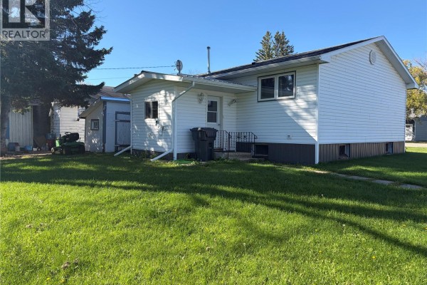 Rear right side of the white vinyl-sided bungalow with a back door and garbage bins. - 403 & 401 Main Street, Pelly