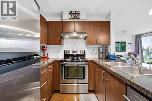 View of a U-shaped kitchen featuring dark wood cabinets, granite countertops, and stainless steel appliances. - 403 12075 228 Street, Maple Ridge